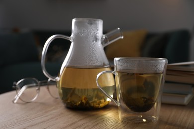 Glass teapot and cup of hot tea on wooden table in living room. Cozy home atmosphere