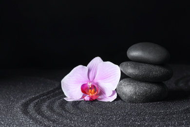 Spa stones and orchid flower on black sand with beautiful pattern, space for text. Zen concept