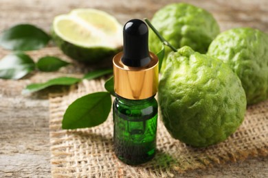 Bottle of essential oil and fresh bergamot fruits on wooden table, closeup