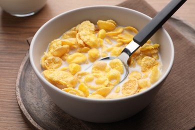 Spoon with tasty cornflakes and milk in bowl on wooden table, closeup