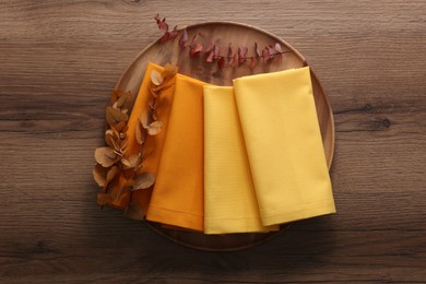 Photo of Tray with different kitchen napkins and decorative dry leaves on wooden table, top view