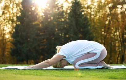 Mature woman practicing yoga on green grass in park
