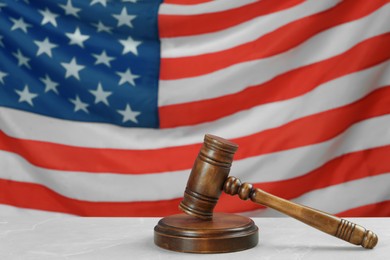 Wooden gavel on light grey table against American flag. Space for text
