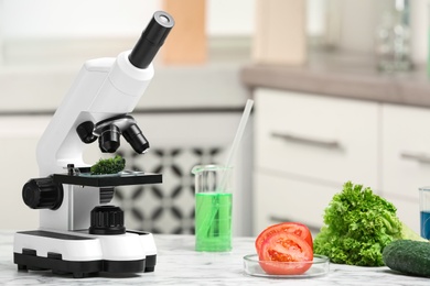 Microscope and fresh vegetables on table in laboratory, space for text. Poison detection