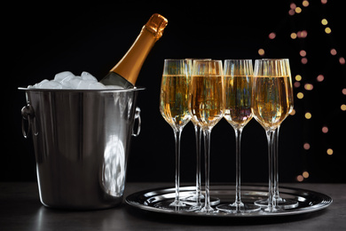 Glasses of champagne and ice bucket with bottle on grey table