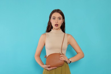 Photo of Emotional young woman in fashionable outfit with stylish bag on light blue background