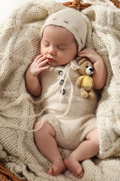 Adorable newborn baby with toy bear sleeping in wicker basket, top view