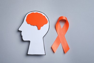 Human head cutout, brain and orange ribbon on grey background, flat lay. Multiple sclerosis concept