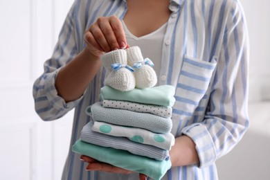 Woman holding stack of baby's clothes and small booties indoors, closeup
