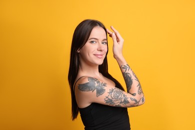 Beautiful woman with tattoos on arm against yellow background