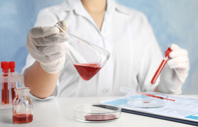 Scientist holding conical flask and tube with blood samples at table, closeup. Virus research