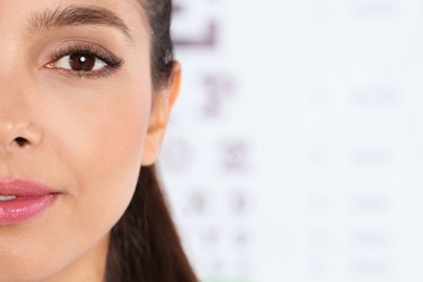 Closeup view of young woman and blurred eye chart on background. Space for text