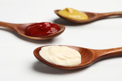 Ketchup, mayonnaise and mustard in spoons on white wooden table, closeup