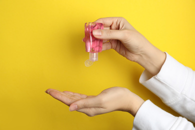 Photo of Woman applying antiseptic gel on hand against yellow background, closeup