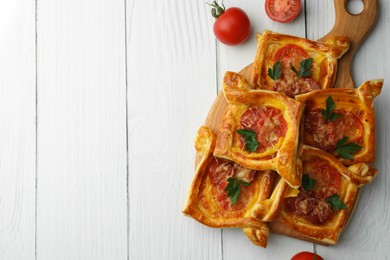 Photo of Fresh delicious puff pastry with cheese, tomatoes and parsley on white wooden table, flat lay. Space for text