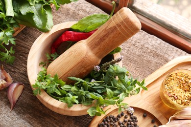 Mortar with pestle, fresh green herbs and different spices on wooden table, above view