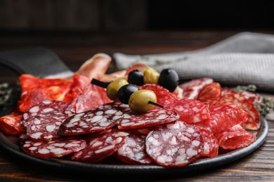 Photo of Tasty salami and other delicacies on wooden table, closeup