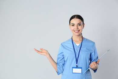 Portrait of young doctor with clipboard against light background