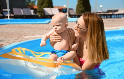 Happy mother with little baby in swimming pool on sunny day