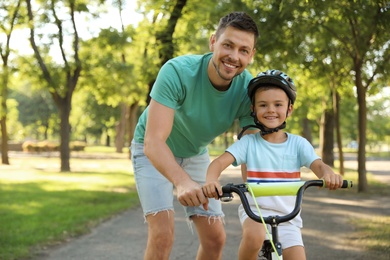 Happy father teaching his son to ride bicycle in park