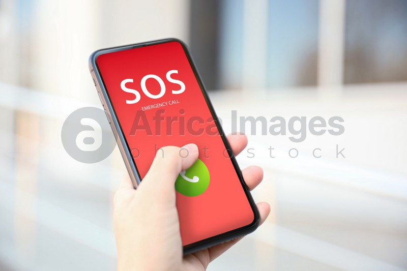 Woman holding smartphone with emergency call SOS on screen outdoors, closeup