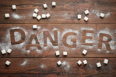 Photo of Flat lay composition with word DANGER and sugar on wooden table