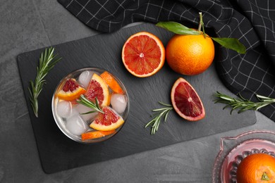 Delicious refreshing drink with sicilian orange and rosemary near fresh ingredients on grey table, flat lay