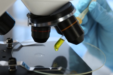 Laboratory assistant doing analysis with urine sample and microscope, closeup