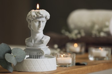 Beautiful David bust candle and eucalyptus branch on wooden table in room, space for text