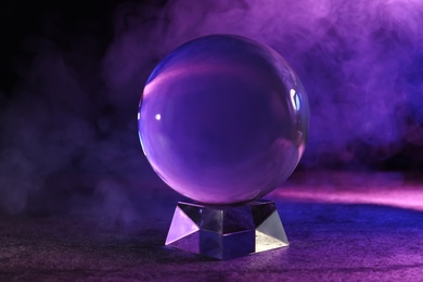 Crystal ball on table and smoke against dark background. Predictions of future