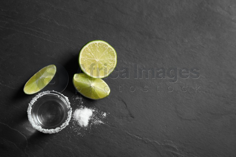Mexican Tequila shot, lime slices and salt on black table, flat lay. Space for text