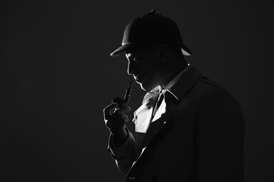 Old fashioned detective with smoking pipe on dark background, black and white effect. Space for text