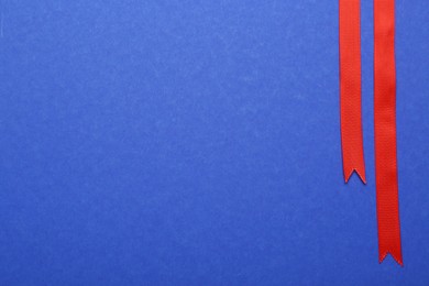 Photo of Beautiful red ribbons on blue background, flat lay. Space for text