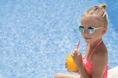 Cute little girl with glass of juice near swimming pool on sunny day. Space for text