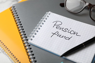 Glasses and notebook with words PENSION FUND on table