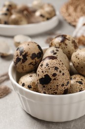 Fresh quail eggs in bowl on light grey table, closeup