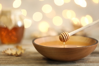 Honey dripping from dipper into bowl on table against blurred lights. Space for text