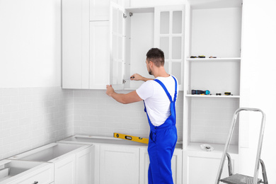 Photo of Worker installing door of cabinet with screwdriver in kitchen