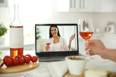Friends drinking wine while communicating through online video conference in kitchen. Social distancing during coronavirus pandemic