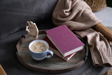 Photo of Wooden tray with books and coffee on armchair indoors