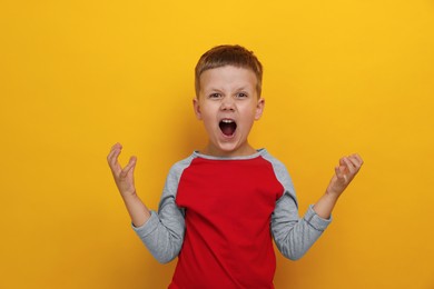 Photo of Angry little boy screaming on yellow background. Aggressive behavior