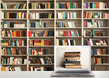 Digital library concept. Modern laptop on table and shelves with books indoors