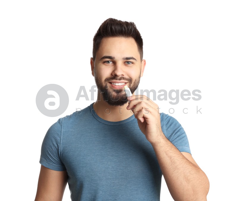 Young man applying lip balm on white background