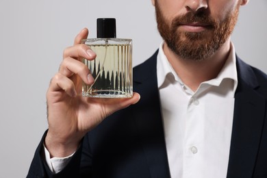 Photo of Handsome bearded man with bottle of perfume on light grey background, closeup