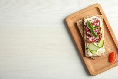 Photo of Fresh rye crispbreads with salami, cream cheese and cucumber on white wooden table, top view. Space for text