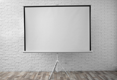 Projection screen near white brick wall indoors. Space for design