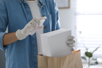 Woman applying antibacterial spray onto package indoors, closeup