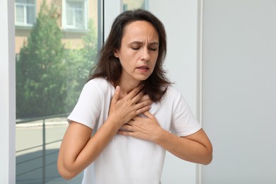 Mature woman suffering from breathing problem near window indoors