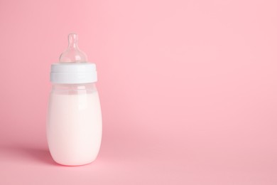 Photo of One feeding bottle with milk on pink background. Space for text