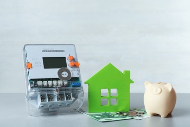 Electricity meter, piggy bank and euro banknotes on grey table